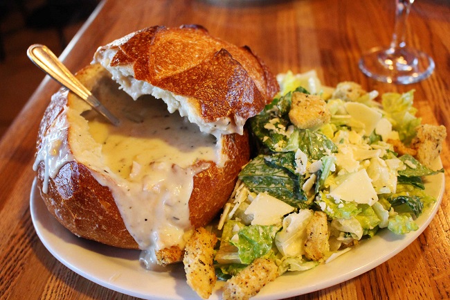 La gustosa zuppa di molluschi servita all'interno di una pagnotta fresca e accompagnata dalla Caesar salad del Pier Market seafo